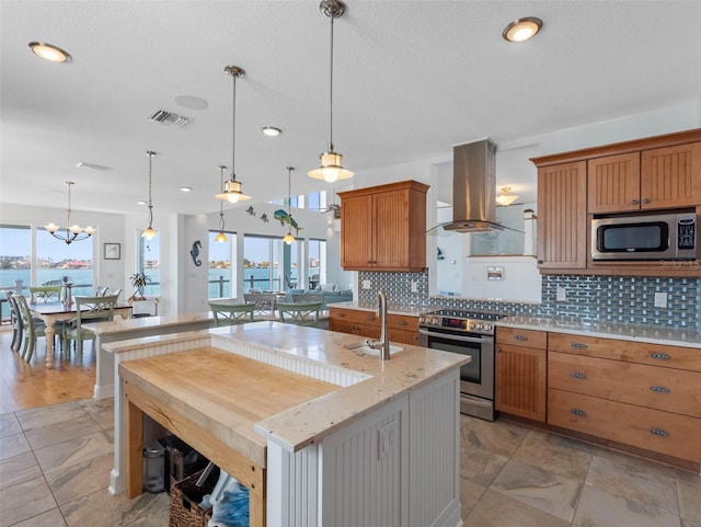 11000 8th St E, Treasure Island, FL 33706 - kitchen with appliances with stainless steel finishes, island range hood, backsplash, decorative light fixtures, and brown cabinets
