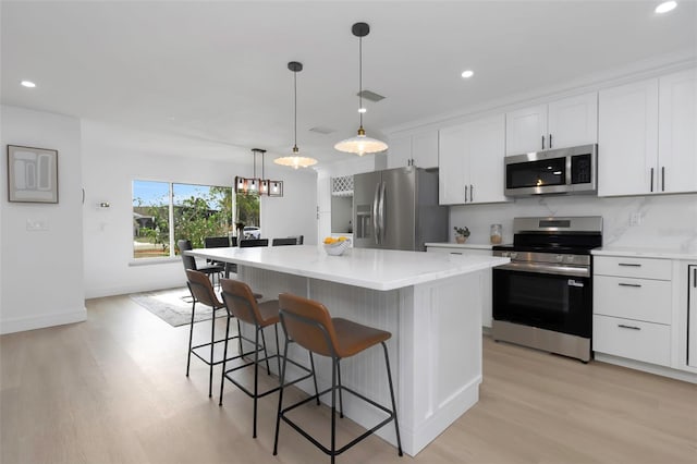 6508 Senegal Palm Way, Apollo Beach, FL 33572 - kitchen featuring appliances with stainless steel finishes, light wood-style floors, a kitchen island, white cabinetry, and a breakfast bar area