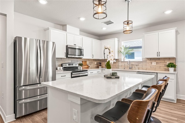 30273 Marquette Ave, Wesley Chapel, FL 33545 - kitchen featuring appliances with stainless steel finishes, white cabinetry, a kitchen island, light wood-style floors, and a breakfast bar area