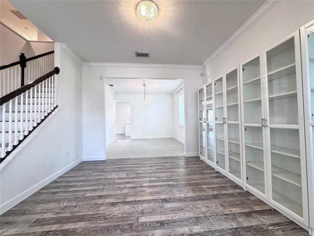 unfurnished room featuring a textured ceiling, wood finished floors, crown molding, baseboards, and a chandelier