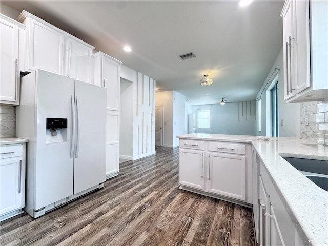 kitchen with white refrigerator with ice dispenser, white cabinets, a peninsula, tasteful backsplash, and dark wood finished floors
