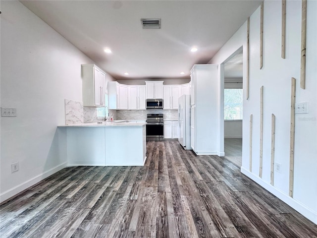 kitchen with appliances with stainless steel finishes, decorative backsplash, dark wood finished floors, a peninsula, and recessed lighting