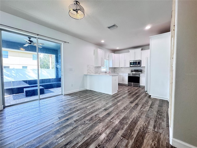 kitchen with stainless steel appliances, dark wood-style floors, a peninsula, backsplash, and recessed lighting