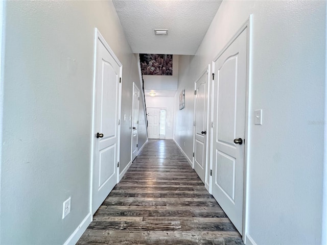 hall featuring a textured ceiling, dark wood-style floors, and baseboards