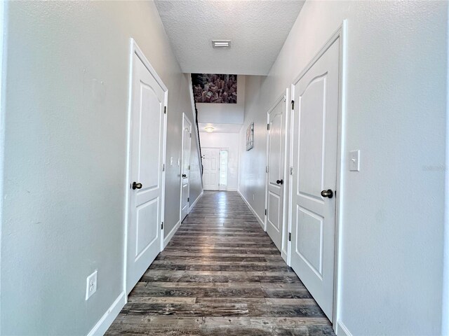 hall featuring a textured ceiling, dark wood-style floors, and baseboards