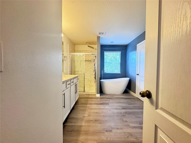 full bathroom featuring a shower stall, vanity, wood finished floors, a textured ceiling, and a soaking tub