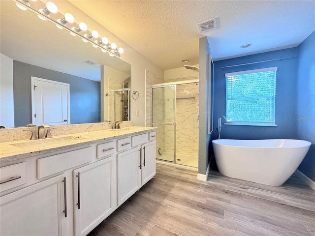 bathroom with a stall shower, double vanity, a freestanding tub, wood finished floors, and a textured ceiling