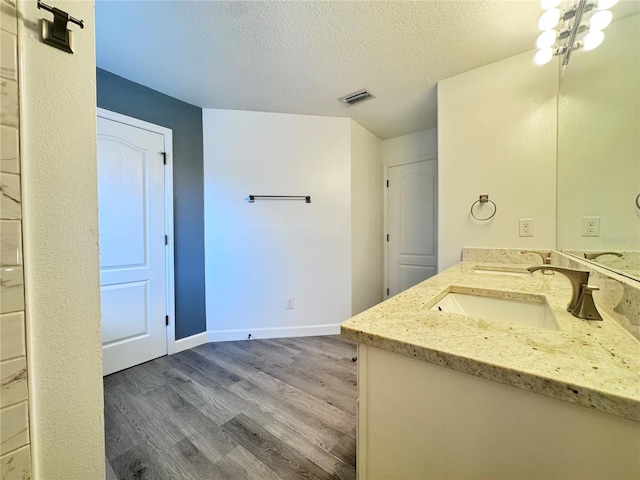 bathroom featuring wood finished floors, a textured ceiling, baseboards, and double vanity