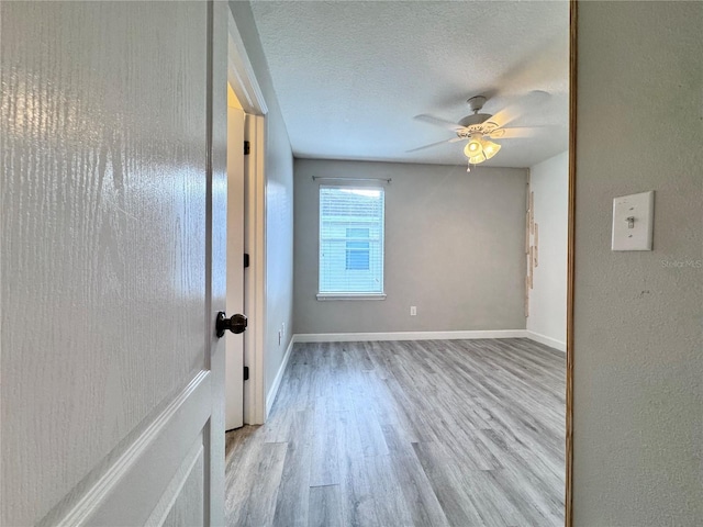 empty room with wood finished floors, a ceiling fan, baseboards, and a textured ceiling