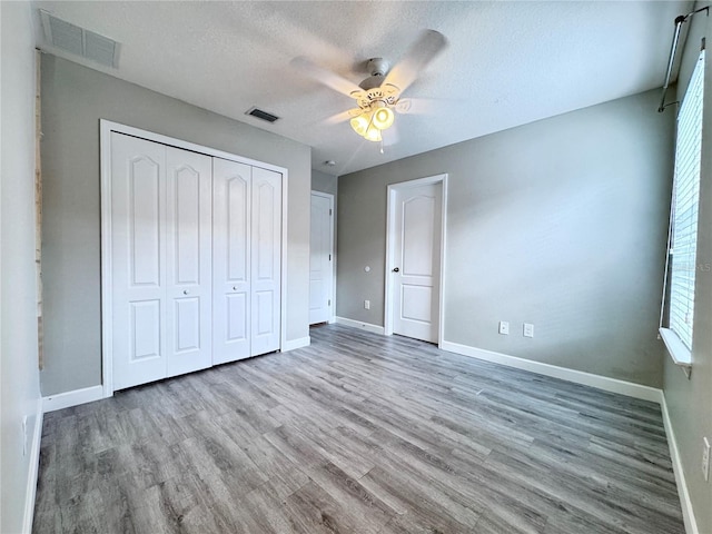 unfurnished bedroom with baseboards, wood finished floors, a textured ceiling, a closet, and a ceiling fan