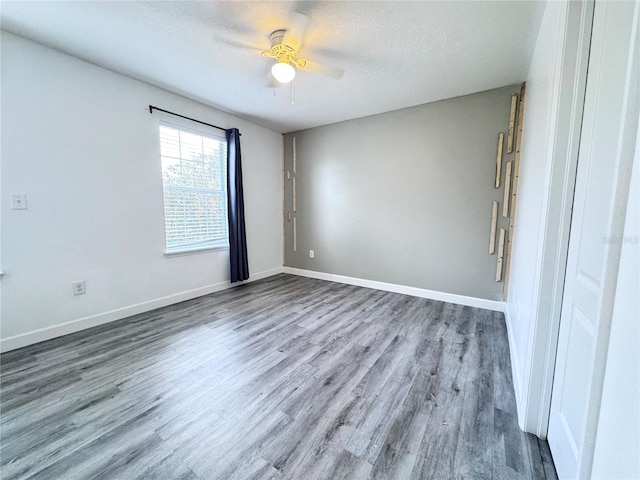 empty room with wood finished floors, a ceiling fan, baseboards, and a textured ceiling