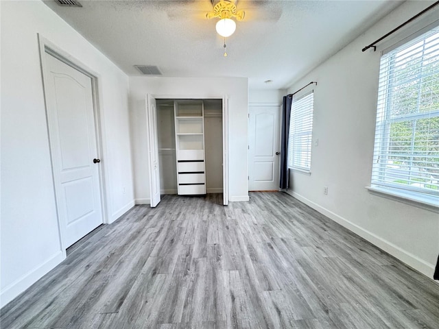 unfurnished bedroom with wood finished floors, baseboards, a textured ceiling, ceiling fan, and multiple closets