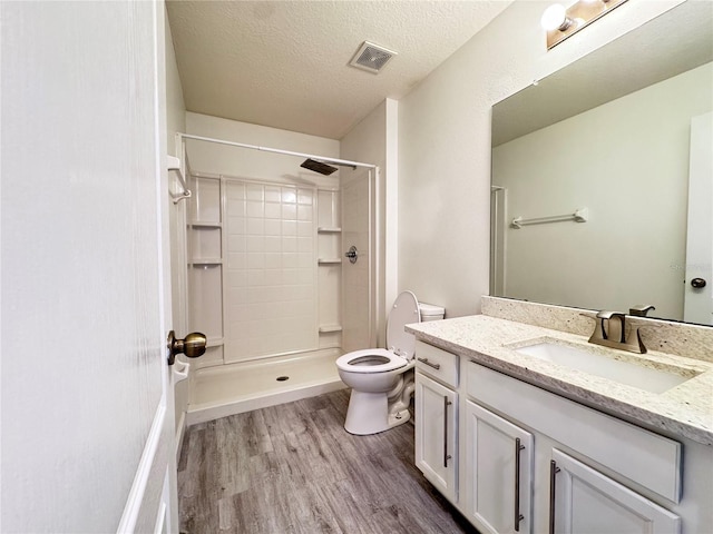 full bathroom featuring wood finished floors, toilet, vanity, a shower, and a textured ceiling
