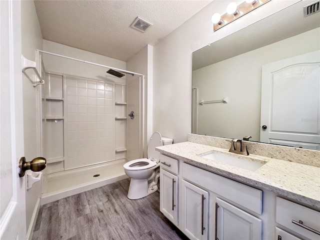 full bathroom with wood finished floors, toilet, vanity, a textured ceiling, and a shower