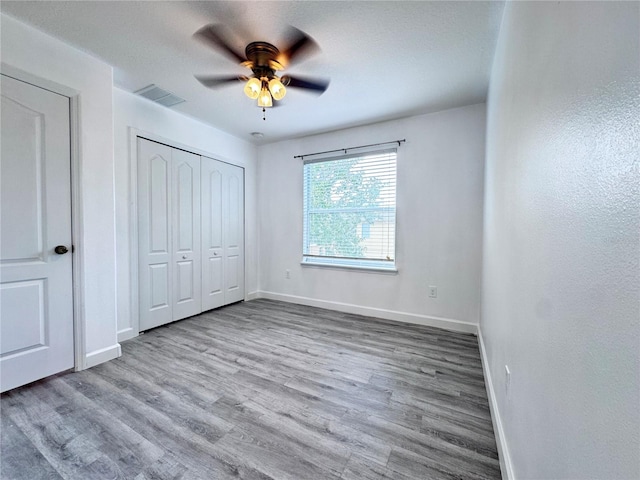 unfurnished bedroom featuring baseboards, wood finished floors, a closet, and a ceiling fan