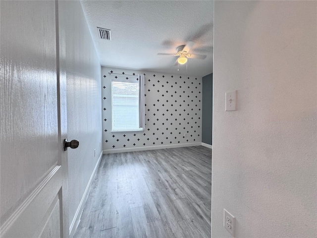 spare room featuring wood finished floors, ceiling fan, baseboards, and a textured ceiling