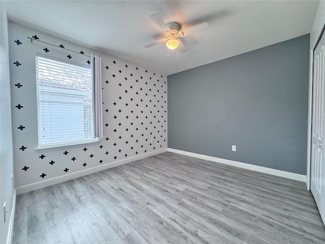 unfurnished room featuring a ceiling fan, a textured ceiling, light wood-style flooring, and baseboards