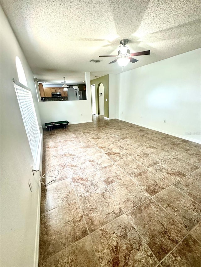 3181 Deltona Blvd, Spring Hill, FL 34606 - unfurnished living room featuring arched walkways, ceiling fan, a textured ceiling, and baseboards