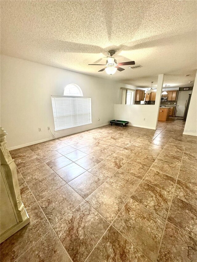 3181 Deltona Blvd, Spring Hill, FL 34606 - unfurnished living room with a textured ceiling, a ceiling fan, baseboards, and dark tile patterned flooring