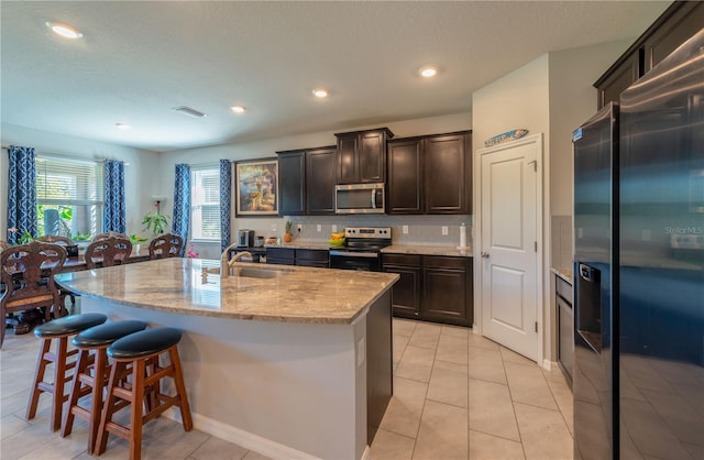 2247 Midnight Pearl Dr, Sarasota, FL 34240 - kitchen featuring appliances with stainless steel finishes, a sink, a breakfast bar area, light stone countertops, and an island with sink