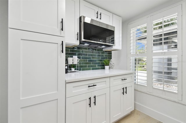 14170 Fennsbury Dr, Tampa, FL 33624 - kitchen featuring stainless steel microwave, backsplash, white cabinetry, and light wood finished floors