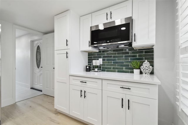 14170 Fennsbury Dr, Tampa, FL 33624 - kitchen featuring stainless steel microwave, light wood-style floors, white cabinetry, light countertops, and decorative backsplash