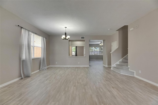 unfurnished living room featuring a chandelier, a ceiling fan, light wood finished floors, baseboards, and stairs