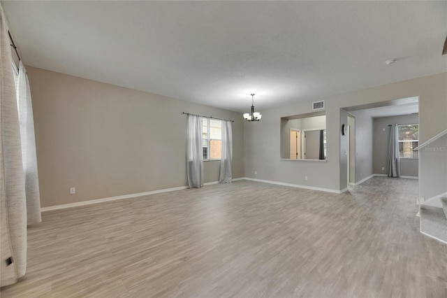 unfurnished living room with a chandelier, light wood-style flooring, stairway, and baseboards