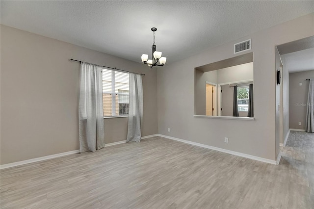 spare room with a chandelier, wood finished floors, baseboards, and a textured ceiling