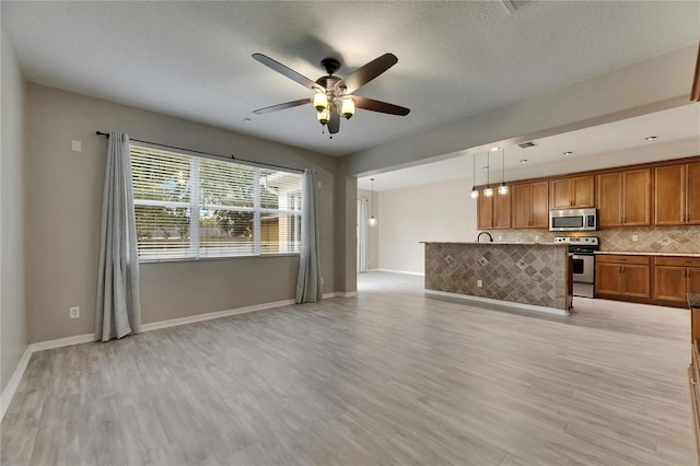 unfurnished living room with a ceiling fan, light wood finished floors, baseboards, and a textured ceiling