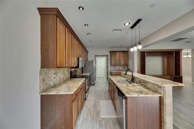 kitchen with appliances with stainless steel finishes, a sink, light wood-style flooring, decorative backsplash, and brown cabinetry