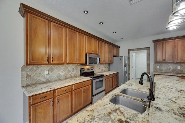 kitchen featuring stainless steel appliances, a sink, brown cabinetry, and light stone countertops