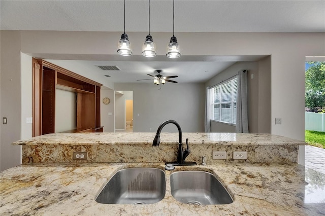 kitchen with a sink, ceiling fan, light stone counters, and pendant lighting