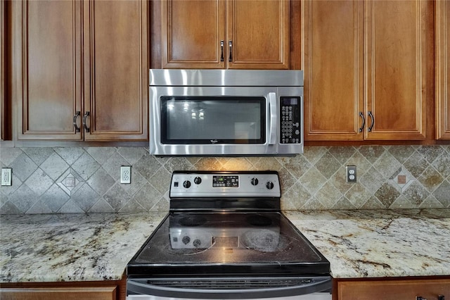 kitchen featuring stainless steel appliances, brown cabinetry, light stone countertops, and backsplash