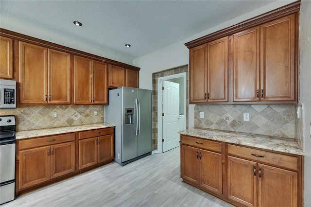kitchen featuring stainless steel appliances, brown cabinetry, light wood-style flooring, backsplash, and a textured ceiling