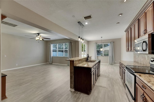 kitchen with stainless steel appliances, a sink, light wood-type flooring, light stone counters, and recessed lighting