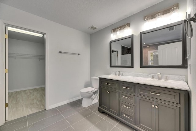 bathroom with tile patterned floors, double vanity, toilet, a spacious closet, and a textured ceiling
