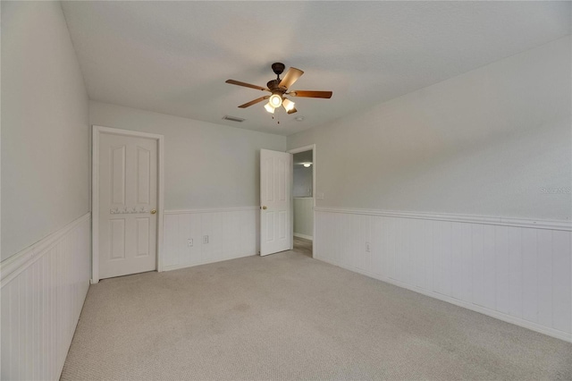 unfurnished bedroom with a wainscoted wall, light carpet, and a ceiling fan