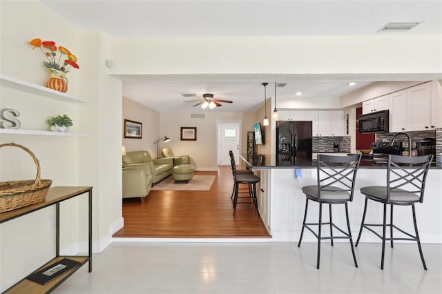 71 Flamingo Cir, Safety Harbor, FL 34695 - kitchen featuring black appliances, dark countertops, a peninsula, a kitchen bar, and white cabinetry