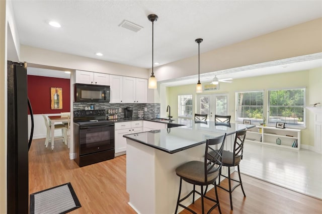71 Flamingo Cir, Safety Harbor, FL 34695 - kitchen with black appliances, a sink, white cabinetry, a peninsula, and a breakfast bar
