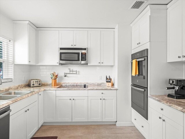 4005 W Coachman Ave, Tampa, FL 33611 - kitchen with appliances with stainless steel finishes, tasteful backsplash, white cabinetry, a sink, and light stone countertops