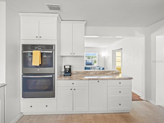 4005 W Coachman Ave, Tampa, FL 33611 - kitchen with stainless steel double oven, white cabinets, light stone counters, and baseboards
