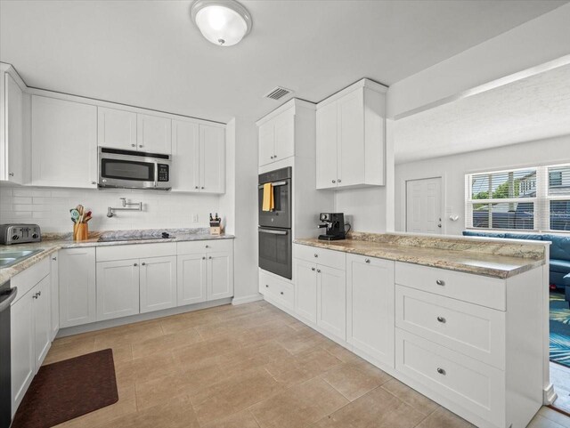 4005 W Coachman Ave, Tampa, FL 33611 - kitchen with black appliances, decorative backsplash, white cabinetry, a peninsula, and light stone countertops