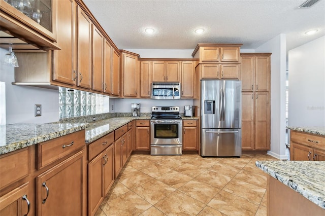 13028 Prestwick Dr, Riverview, FL 33579 - kitchen with appliances with stainless steel finishes, brown cabinets, a textured ceiling, light stone counters, and recessed lighting