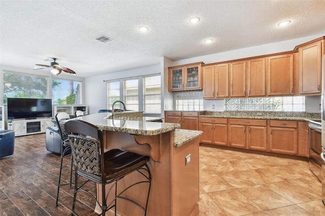 13028 Prestwick Dr, Riverview, FL 33579 - kitchen with a kitchen breakfast bar, brown cabinetry, a ceiling fan, a textured ceiling, and recessed lighting