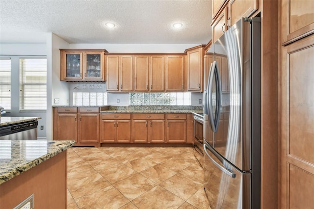 13028 Prestwick Dr, Riverview, FL 33579 - kitchen with appliances with stainless steel finishes, a textured ceiling, brown cabinets, light stone countertops, and glass insert cabinets