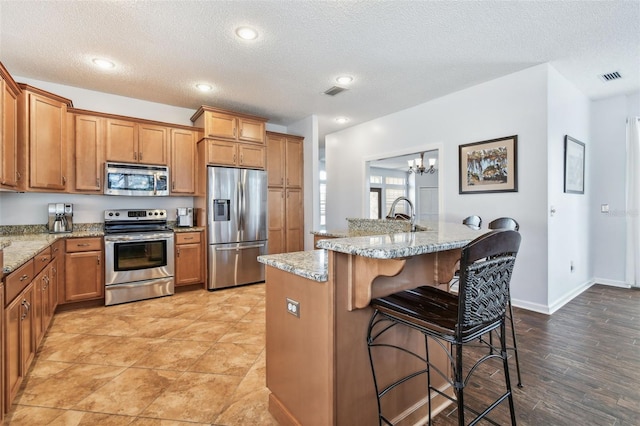13028 Prestwick Dr, Riverview, FL 33579 - kitchen with appliances with stainless steel finishes, brown cabinetry, a breakfast bar area, a textured ceiling, and light stone countertops