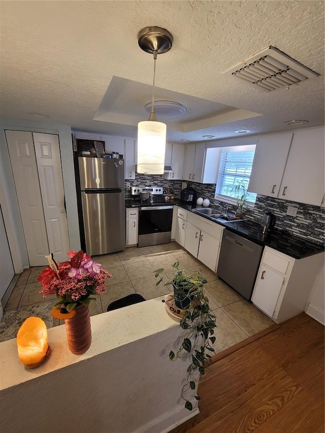 kitchen with appliances with stainless steel finishes, dark countertops, white cabinetry, decorative backsplash, and a textured ceiling