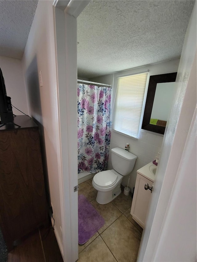 bathroom with a textured ceiling, vanity, toilet, tile patterned floors, and curtained shower