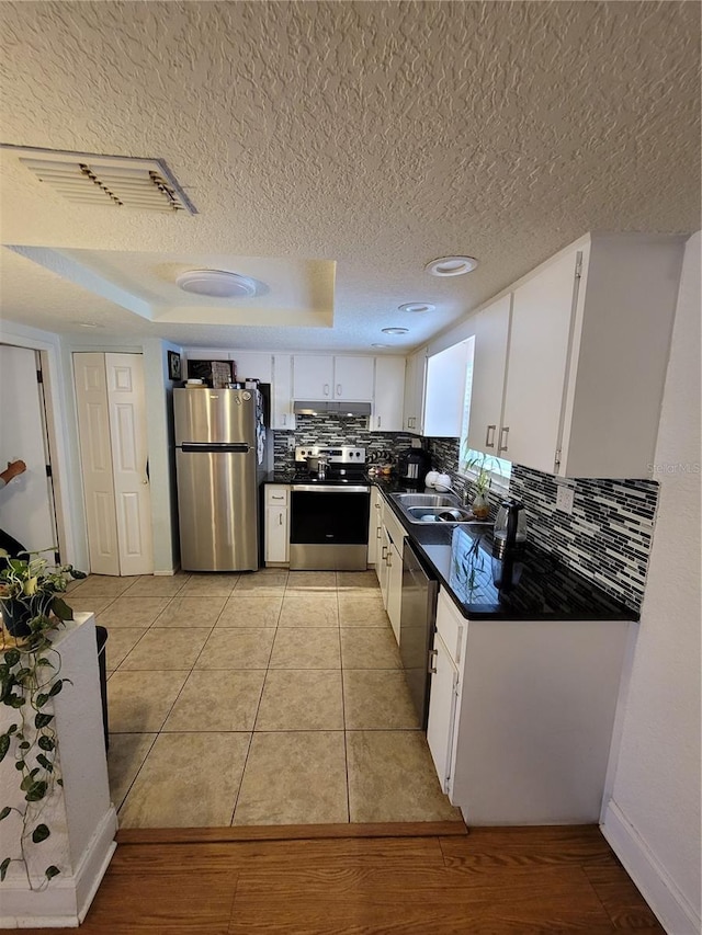kitchen with appliances with stainless steel finishes, dark countertops, tasteful backsplash, a textured ceiling, and white cabinets